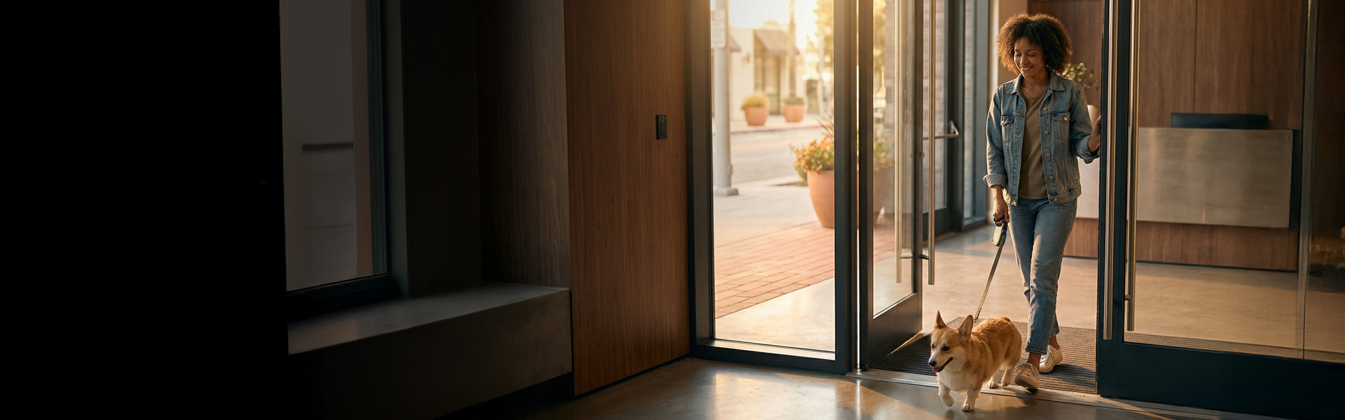 A woman and a small dog walking thru the entrance of a building.